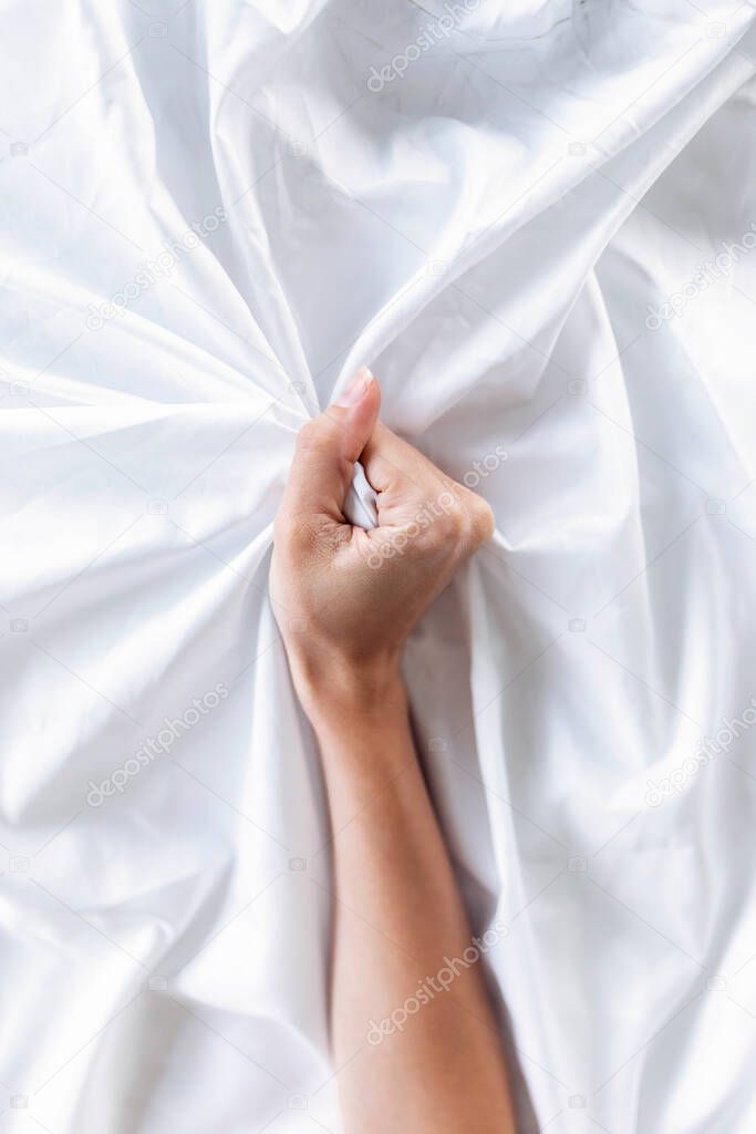 Close-up of woman's hand holding a satin white sheet. Pleasure concept.