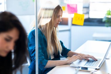 İki iş kadınının ortak çalışma alanındaki bölümlü masada dizüstü bilgisayarlarla çalışırken çekilmesi. Sosyal uzaklık kavramı.