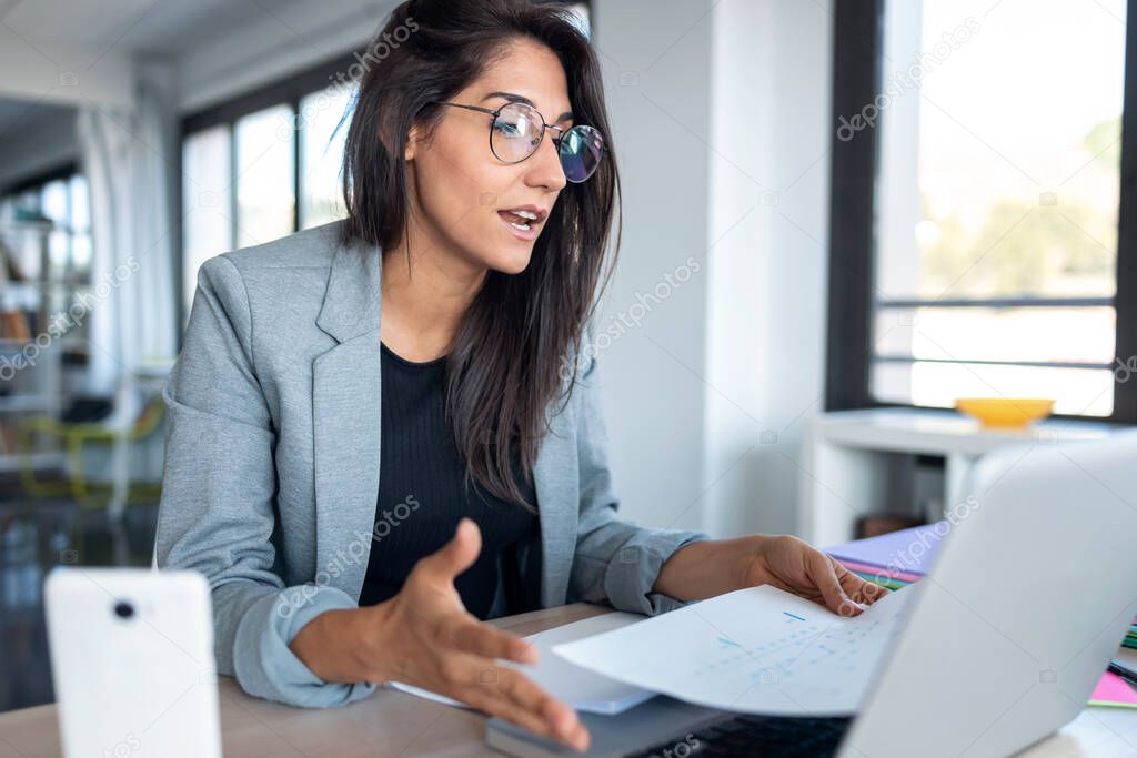 Shot of confident business woman looking and speaking through the webcam while making a video conference with laptop from the office.