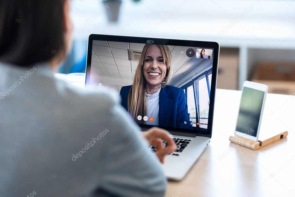 Back view of female employee speaking on video call with her colleague on online briefing with laptop at home.