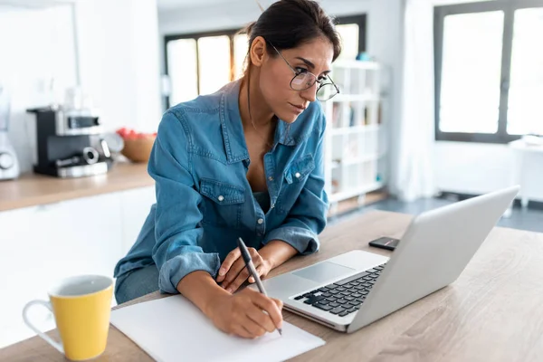 Tiro Mulher Muito Jovem Escrevendo Notas Trabalhando Laptop Cozinha Casa — Fotografia de Stock