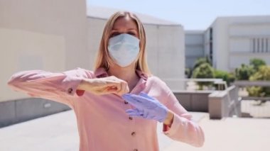 Güzel sarışın bir kadının koruyucu eldivenlerini ve maskesini çıkardığı ve sokakta temiz havanın tadını çıkardığı bir video..