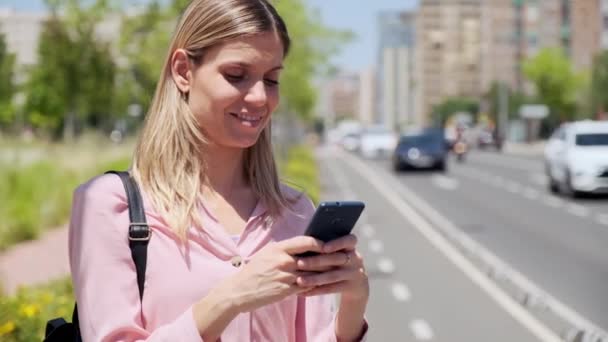 街の通りに立っている間に彼女の携帯電話を使用して美しいですブロンド女性のビデオ — ストック動画