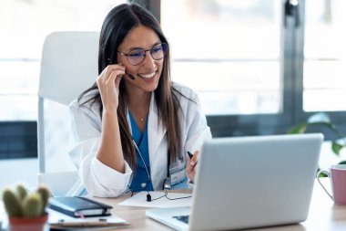 Konsültasyondaki bir bilgisayarla iş arkadaşlarıyla görüntülü konuşma yapan kadın doktor..