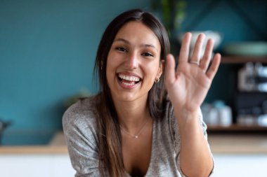 Evdeki mutfaktaki dizüstü bilgisayardan gülümseyen genç bir kadının fotoğrafı..