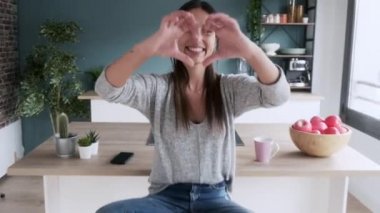 Evdeki mutfakta elleri ile kalp şekli alırken kameraya bakan güzel bir genç kadının videosu..