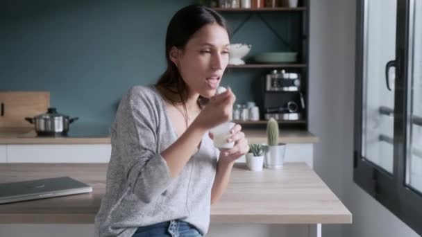 Evdeki Mutfaktaki Taburede Otururken Yoğurt Yiyen Gülümseyen Genç Kadının Videosu — Stok video