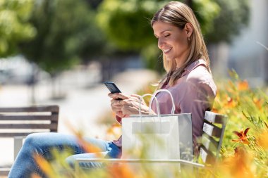 Güzel sarışın bir kadının sokakta bankta otururken cep telefonunu kullanması..
