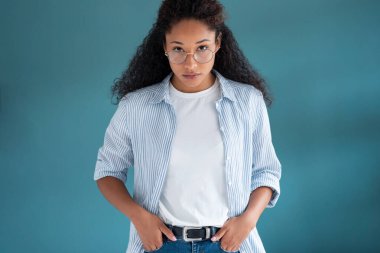Mavi arka planda poz verirken ciddi bir ifadeyle kameraya bakan güzel Afro-Amerikan kadının portresi.
