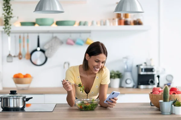 Evdeki Mutfakta Salata Yerken Güzel Bir Genç Kadının Cep Telefonunu — Stok fotoğraf