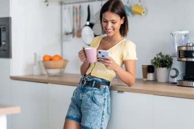 Evdeki mutfakta bir fincan kahve içerken genç ve güzel bir kadının cep telefonunu kullanması..