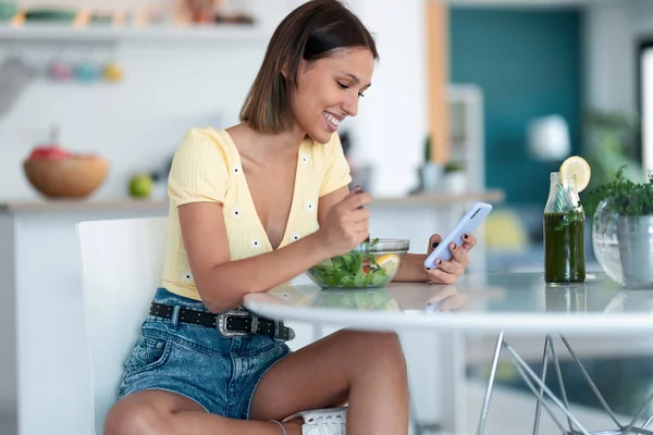 Evdeki Mutfakta Cep Telefonuyla Mesajlaşırken Bir Kase Salata Yiyen Güzel — Stok fotoğraf