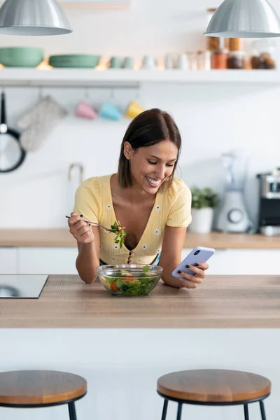 Evdeki Mutfakta Salata Yerken Güzel Bir Genç Kadının Cep Telefonunu — Stok fotoğraf