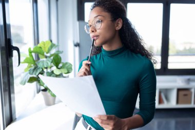 Ofisteki pencereden bakarken konsantre olmuş genç bir kadının bazı belgeleri okuması..