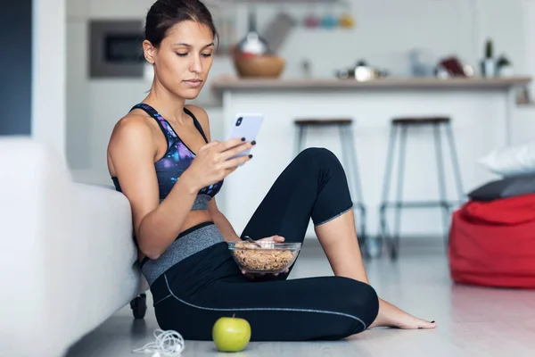 Evde Yerde Oturmuş Cep Telefonuyla Mesajlaşırken Bir Kase Müsli Yiyen — Stok fotoğraf