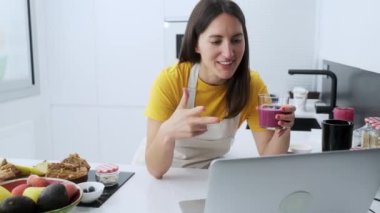 Güzel bir genç beslenme uzmanının bir arkadaşıyla bilgisayardan yaptığı video ile evdeki mutfakta el yapımı detoks smoothie 'yi gösteriyor..
