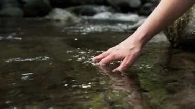 Kadın ellerinin dağdaki bir gölün suyuna dokunduğu ve ıslattığı yakın çekim videosu..