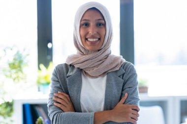 Ofiste dikilirken kameraya bakan tesettürlü genç Müslüman iş kadını portresi.