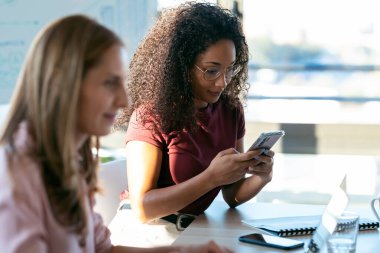 Ofiste meslektaşı ile çalışırken kendine güvenen Afrikalı bir iş kadınının cep telefonuyla mesaj göndermesi..