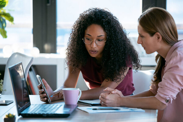 Shot of two beautiful business women working together with laptop while talking about job news in the office.