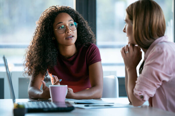 Shot of two beautiful business women working together with laptop while talking about job news in the office.