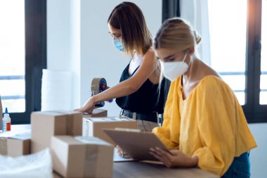 Başlangıçtaki küçük işletmelerinde karton kutuları paketleyip mühürlerken ve ürün siparişini kontrol ederken hijyenik yüz maskesi takan iki güzel serbest çalışan kadın fotoğrafçısı.. 