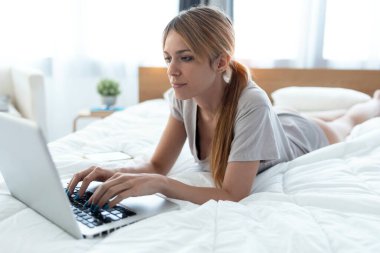 Evdeki yatakta yatarken bilgisayarını kullanan güzel bir kadının fotoğrafı..
