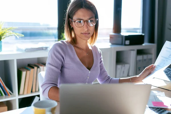 自宅のオフィスでいくつかの文書をコンサルティングしながら コンピュータを操作する集中若いビジネス女性のショット — ストック写真