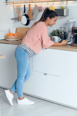 Evdeki mutfakta bir fincan kahve içerken gülümseyen genç bir kadının fotoğrafı..