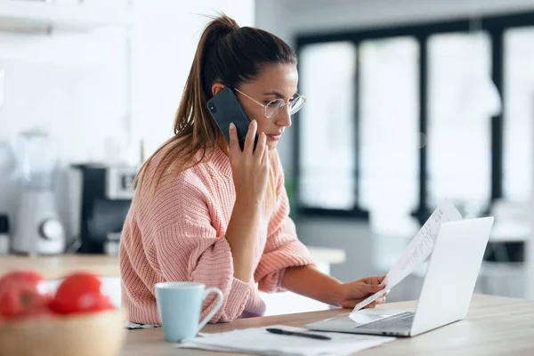 Evde Mutfakta Akıllı Telefonla Konuşurken Bilgisayarla Çalışan Konsantre Genç Bir — Stok fotoğraf