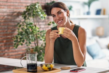 Güzel bir kadının evdeki mutfaktaki kameraya bakarken el yapımı kahve içmesi.