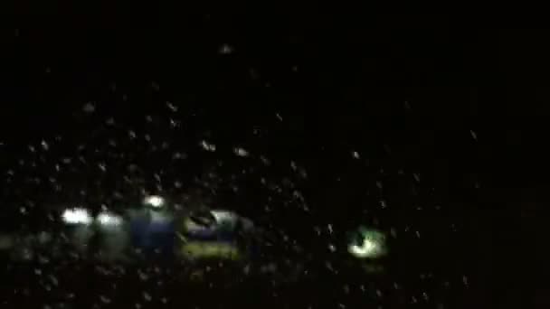 Σταγόνες βροχής σε ένα παράθυρο αυτοκινήτου με θαμπό φόντο του δρόμου τη νύχτα — Αρχείο Βίντεο