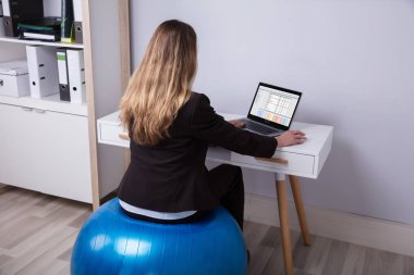 Ofiste çalışan Fitness topu üzerinde oturan bir iş kadını arkadan görünüş