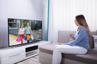 Evde televizyon izlerken hesap makinesini kullanarak kanepe yatan kadın