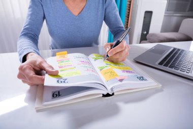 Close-up Of A Woman Writing Schedule In Calendar Diary On White Desk clipart