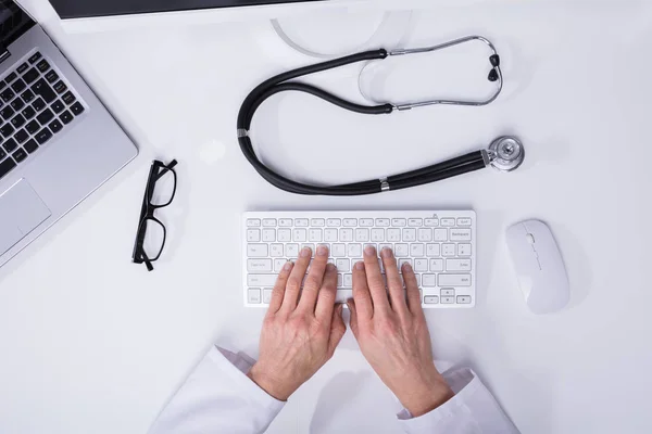 医生的手打字的高视图在电脑键盘与听诊器在书桌上 — 图库照片