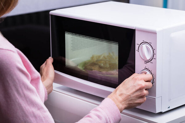 Крупный план женщины, использующей микроволновую печь для обогрева пищи дома
