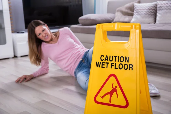 成熟女子跌倒在潮湿的地板在警告前面牌子在家 — 图库照片