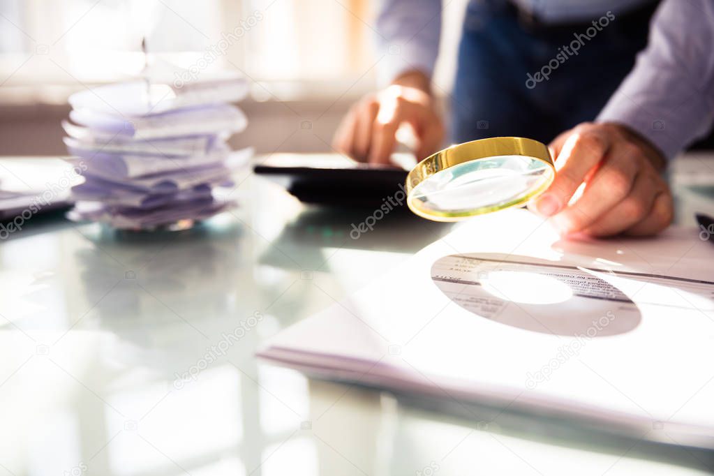 Businessperson's Hand Analyzing Bill Through Magnifying Glass