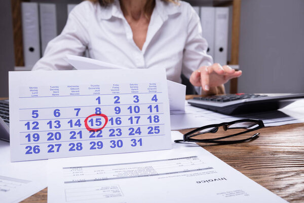 Close-up Of Calendar And Invoice In Front Of Businessperson Working At Workplace
