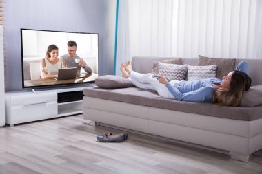 Evde televizyon izlerken hesap makinesini kullanarak kanepe yatan kadın