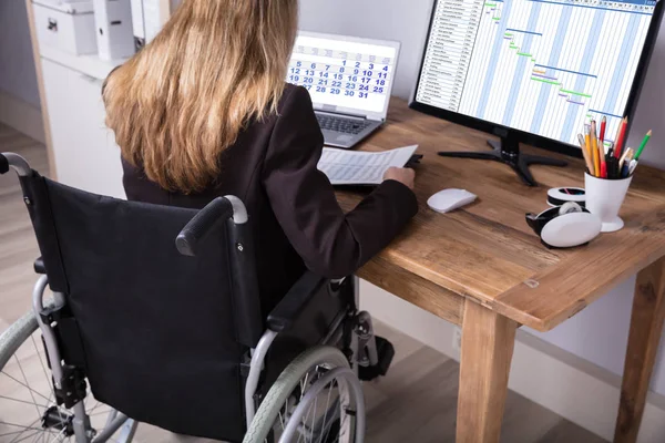 Rear View Of A Disabled Businesswoman Sitting On Wheelchair Working On Computer