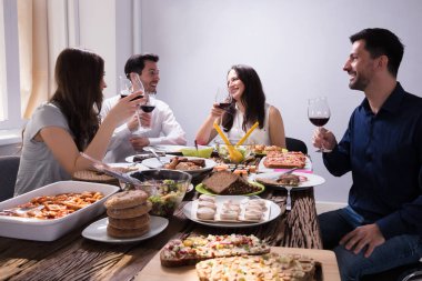 Smiling Young Friends Enjoying Food With Glass Of Wine At Restaurant clipart