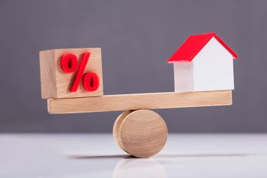 Ahşap tahterevalli yüzde sembolü ve ev modeli arasında denge gösterilen Close-Up