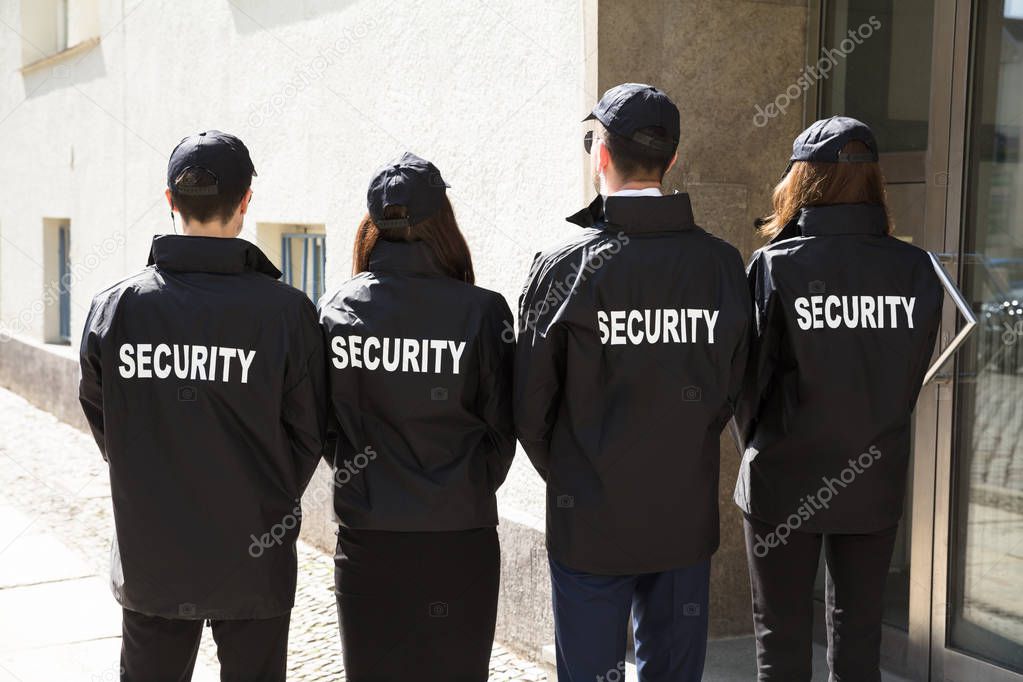Rear View Of Security Guards Wearing Uniform Standing In A Row