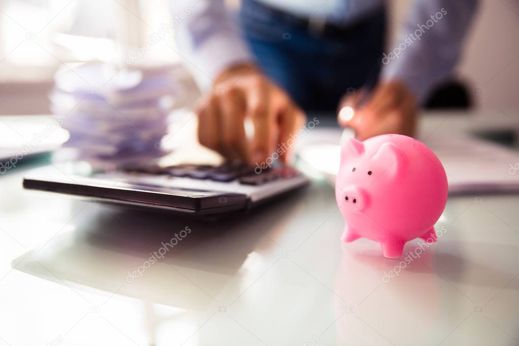 Close-up Of Pink Piggybank Near Businessperson's Hand Using Calculator