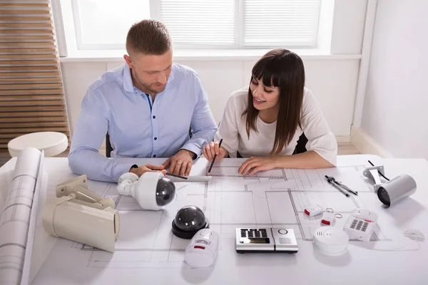Two Architects Working On Blueprint With Security Equipments On Desk