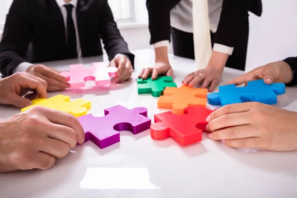 机の上の色とりどりのジグソー パズルを解くの実業家のグループ — ストック写真