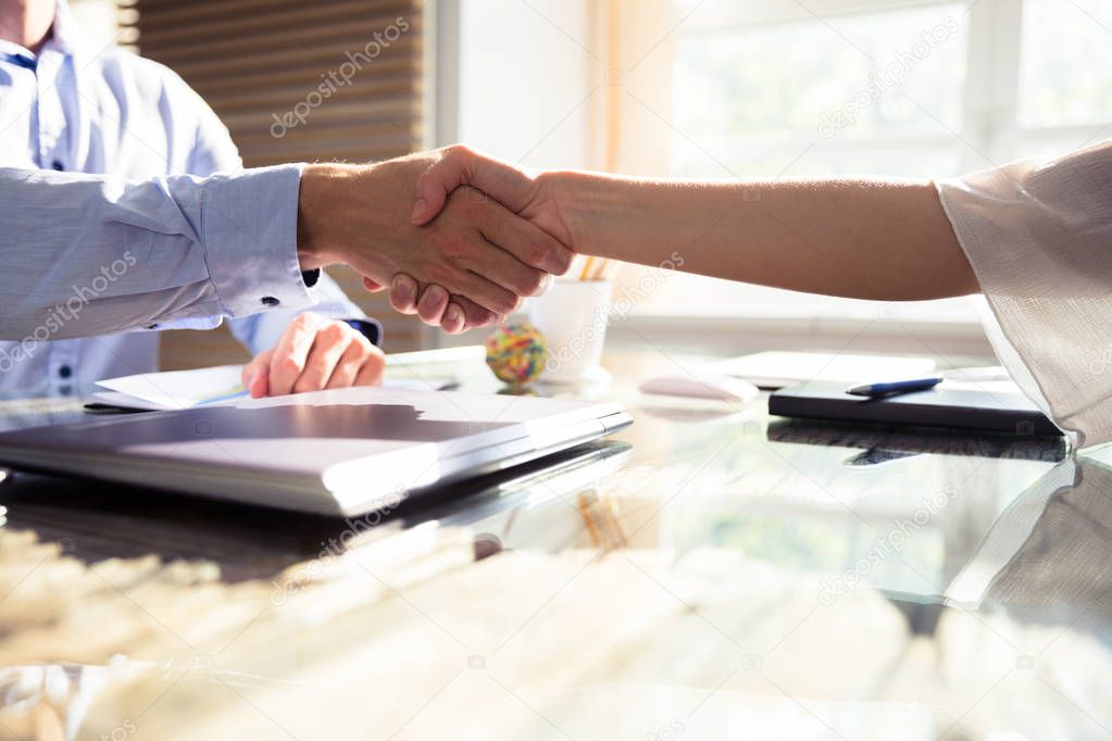 Close-up Of Two Business Partners Shaking Hands Over Desk In Office