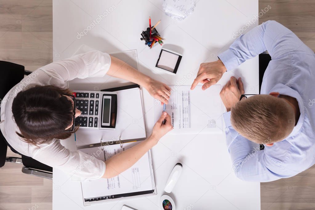 High Angle View Of Two Businesspeople Analyzing Bill In Office